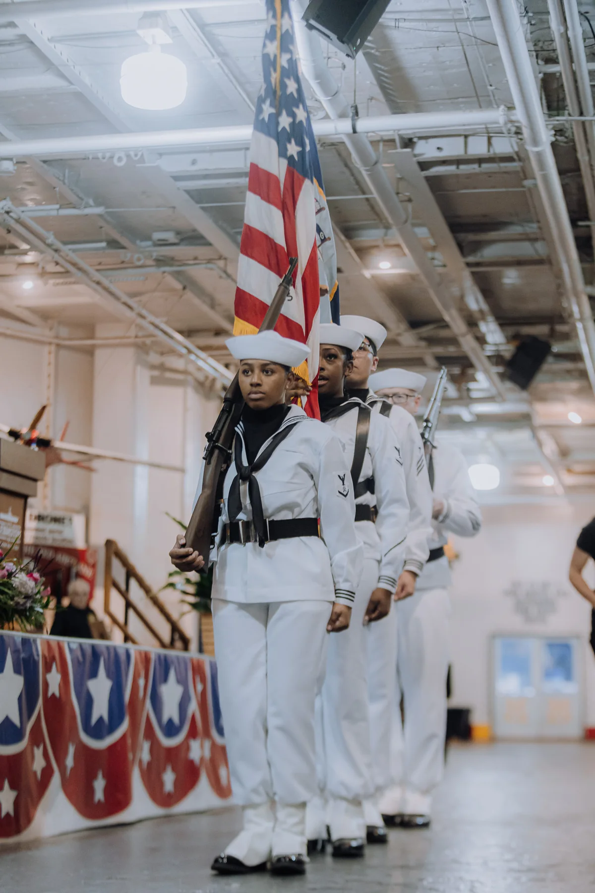Sailors walking in formation inside a decorated venue